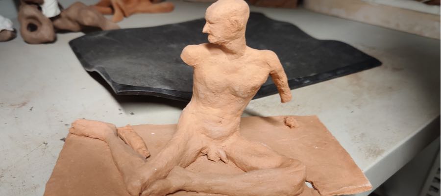 A clay sculpture of a male nude in a yoga-like seated position with missing arms.