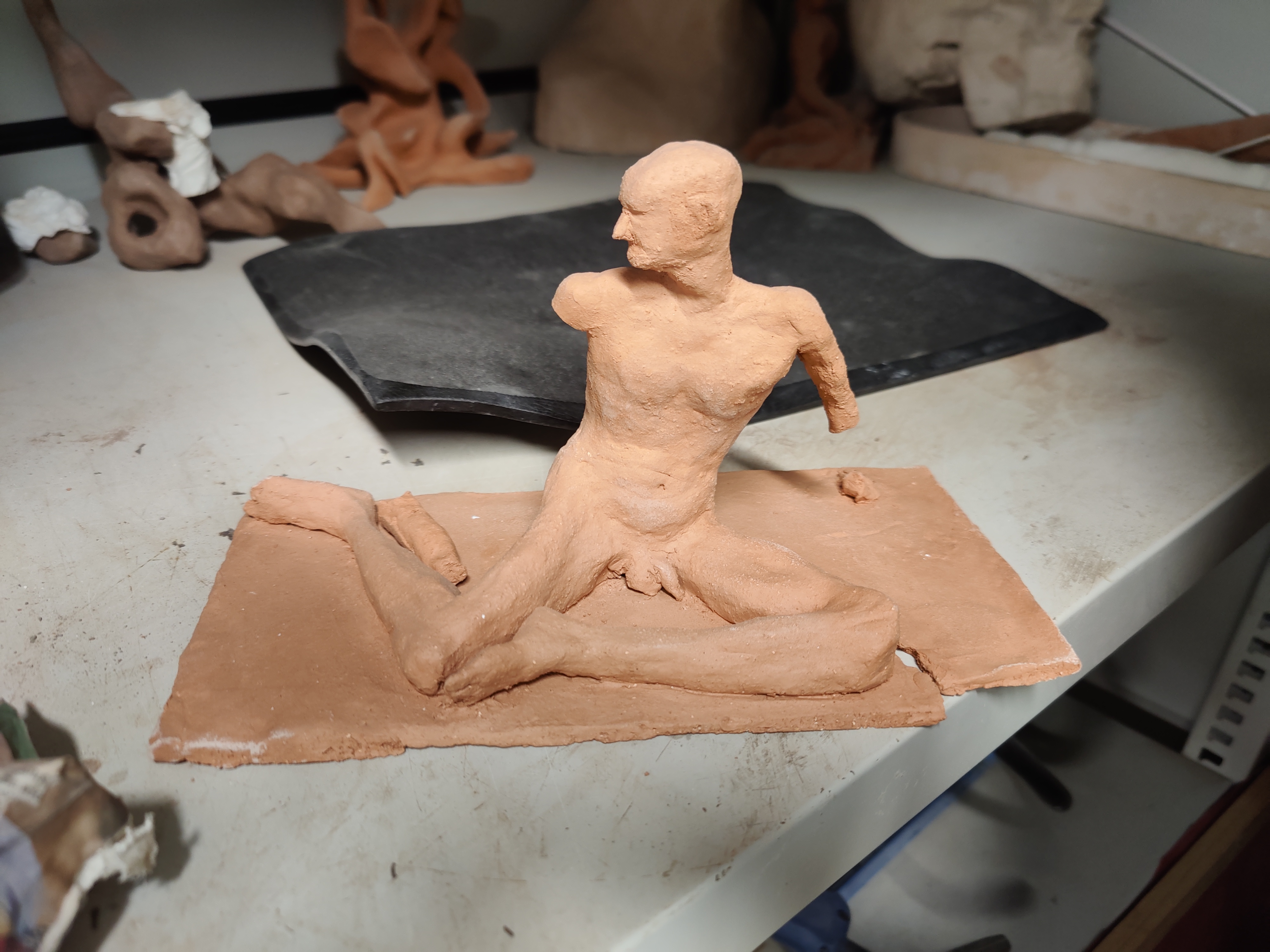 Terracotta fired clay statue of a man sitting upright with legs bent at 90 degrees to form a triangle, and no arms