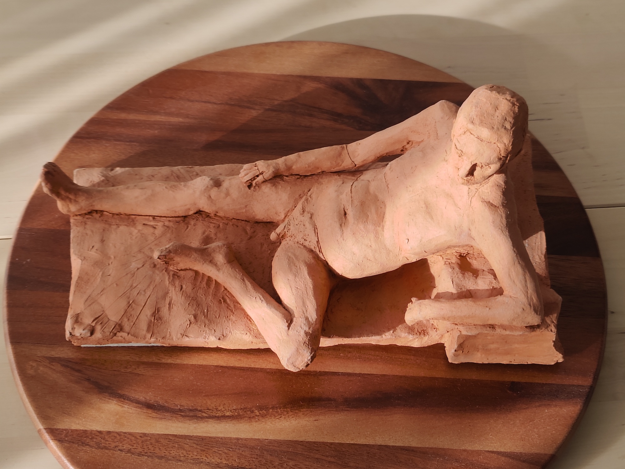 Bisque-fired figurative sculpture of a nude man reclining in terracotta clay