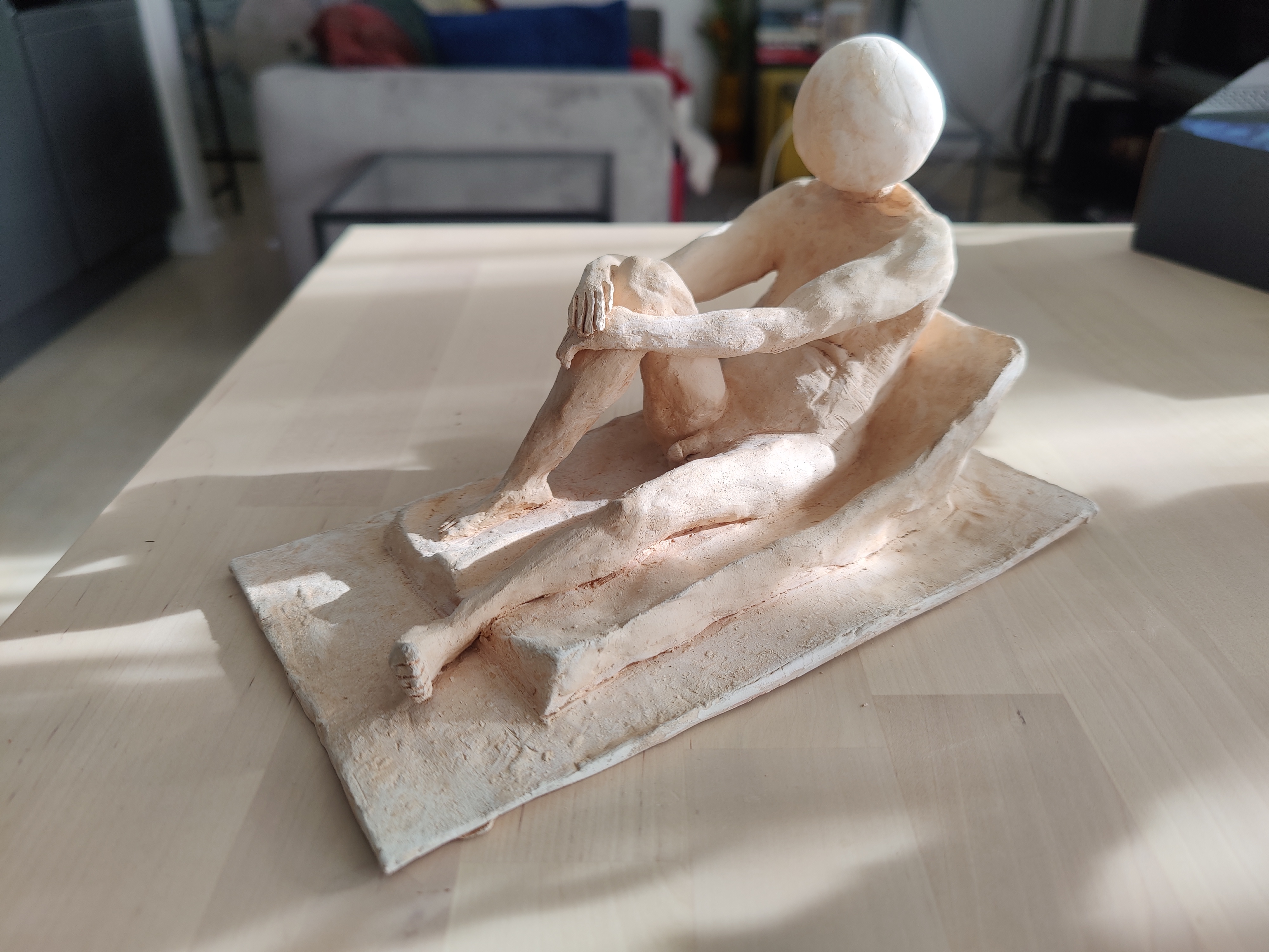 Clay sculpture of a seated male nude with a sphere for a head