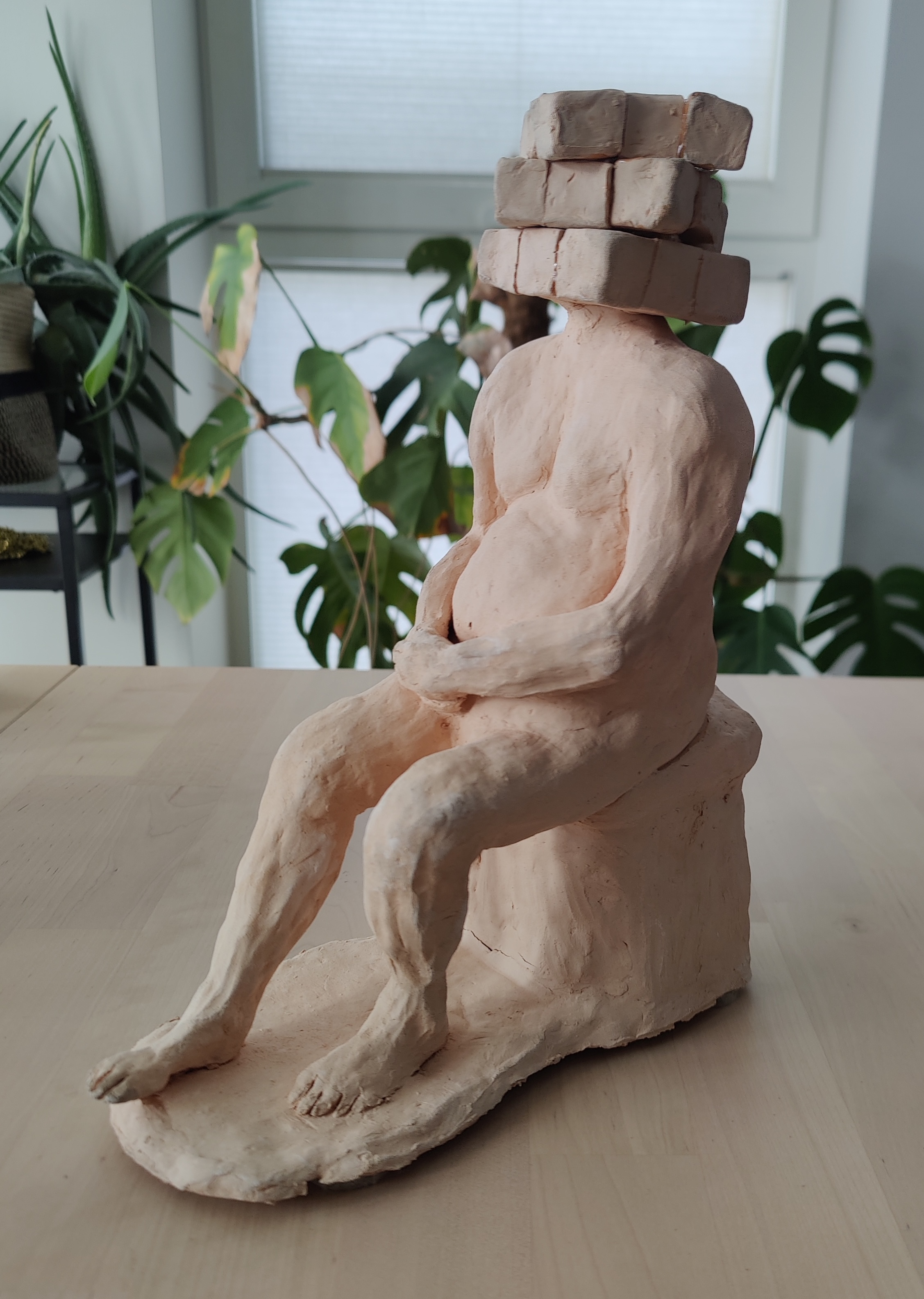 Clay sculpture of an ambiguously gendered seated person with a Rubik's cube for a head