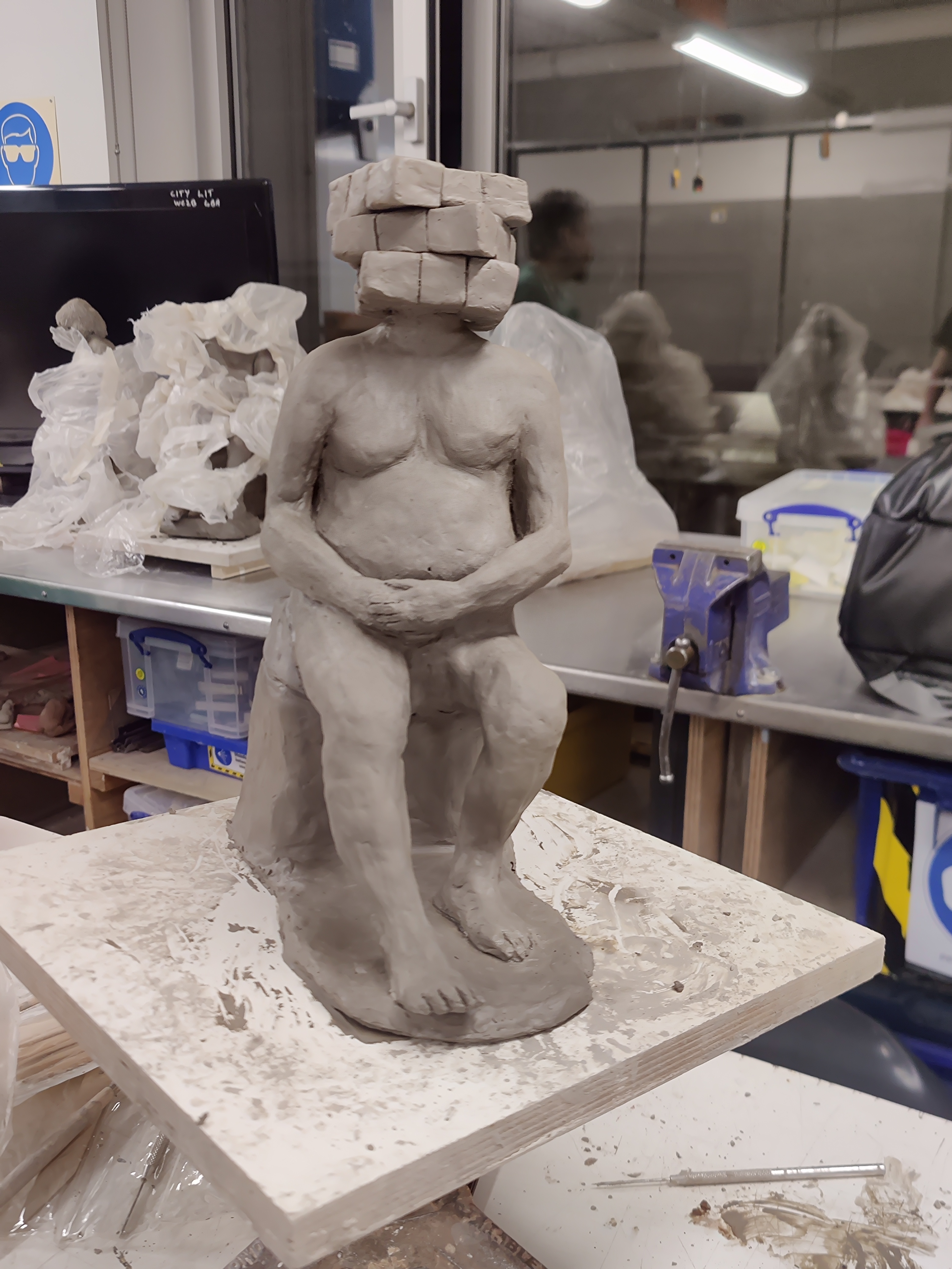 Grey clay sculpture of a seated man with a Rubik's Cube for a head